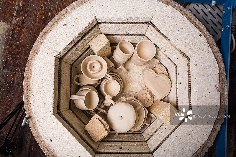 陶瓷，车间，陶瓷艺术概念-小型电炉进一步焙烧未完成的粘土产品，窑为杯子和未焙的水壶，平铺，俯视图图片素材
