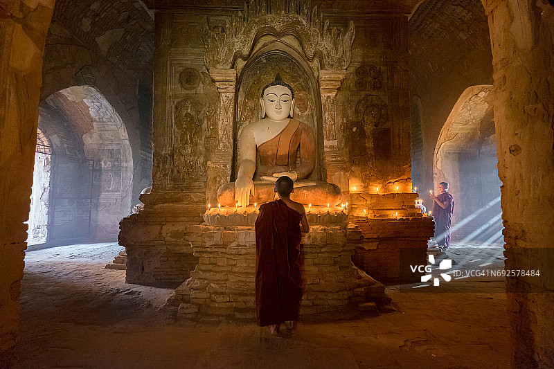 年轻的小沙僧在蒲甘老塔内的佛像前用蜡烛祈祷图片素材
