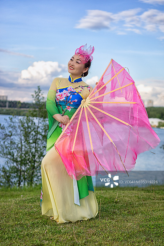 美丽的中国女孩穿着传统的中国服装，拿着扇子在河岸上图片素材
