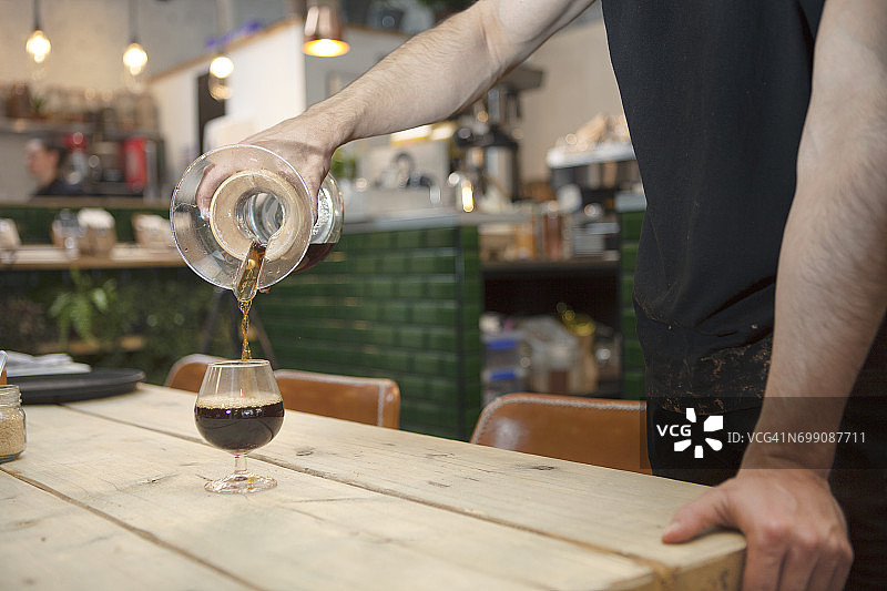 男咖啡师的手倒黑咖啡到白兰地杯在咖啡馆图片素材