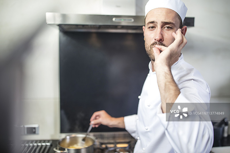 厨师在炉子上搅拌平底锅的肖像，用手指对着嘴唇发信号图片素材