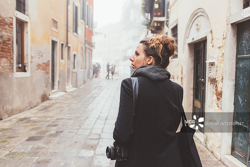 意大利威尼斯，年轻女子拿着相机在街上回头看图片素材