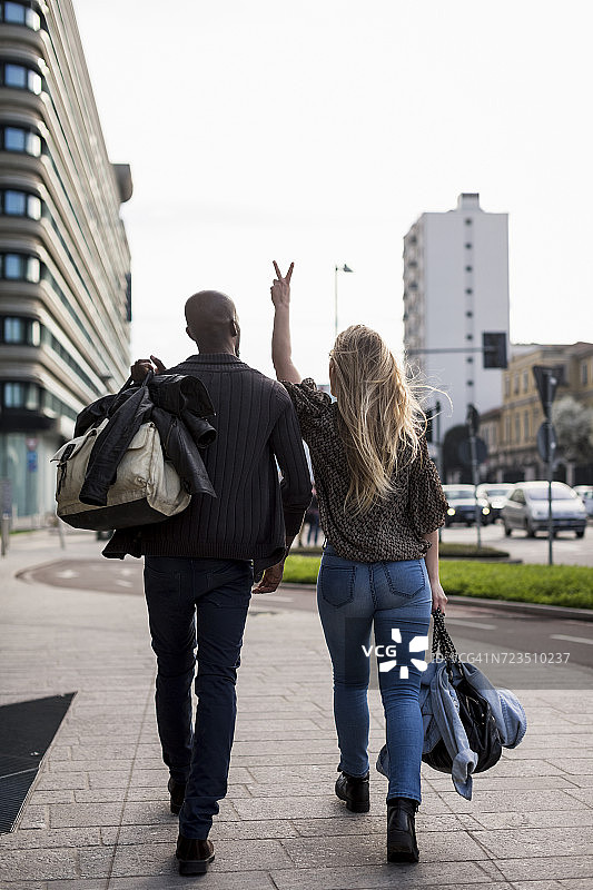 年轻夫妇在城市人行道上做和平标志的后视图图片素材