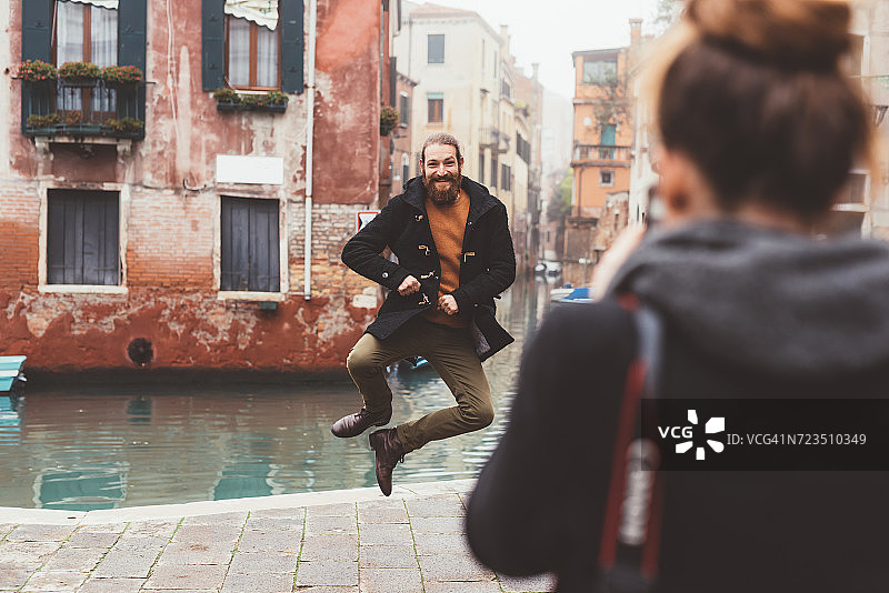 意大利威尼斯，一名女子拍摄一名男子在运河上跳跃图片素材