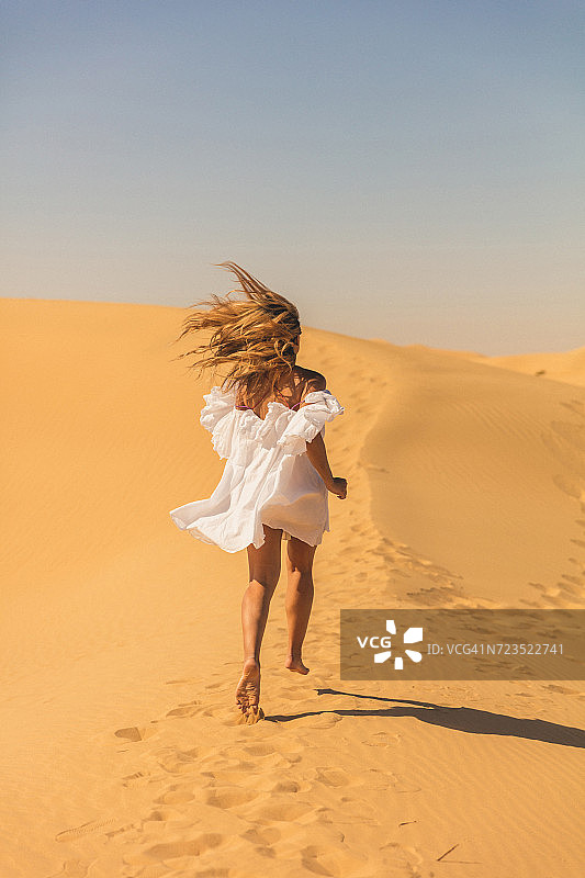"一个女人在迪拜的沙丘里奔跑的后视镜"图片素材