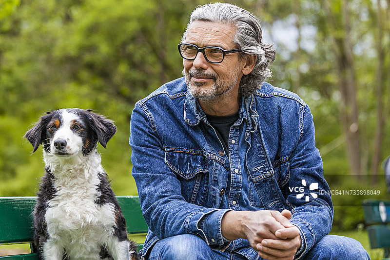 一个灰白头发和胡子的男人坐在他的狗旁边的长凳上图片素材