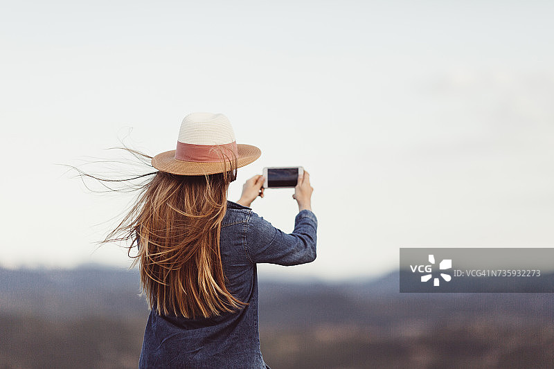 红发女人用智能手机在大自然中拍照的背影图片素材