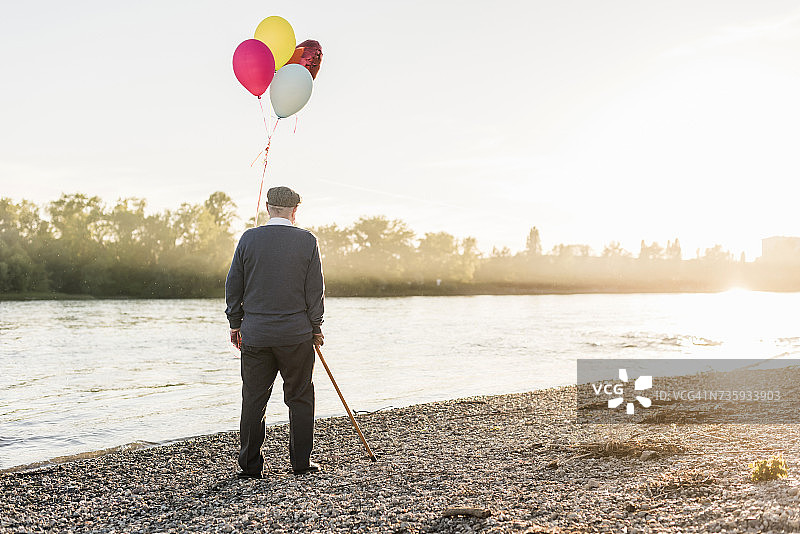 傍晚时，老男人带着气球站在河边的背影图片素材