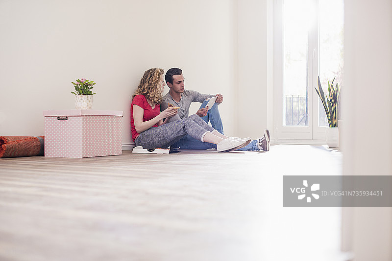 一对年轻夫妇在新家里坐在地板上，手里拿着平板电脑图片素材