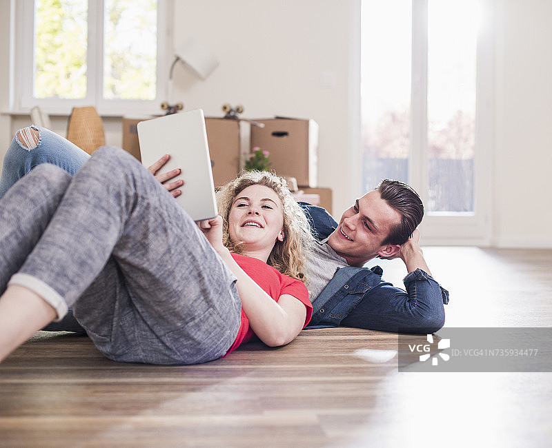幸福的年轻夫妇在新家的地板上躺着平板电脑图片素材