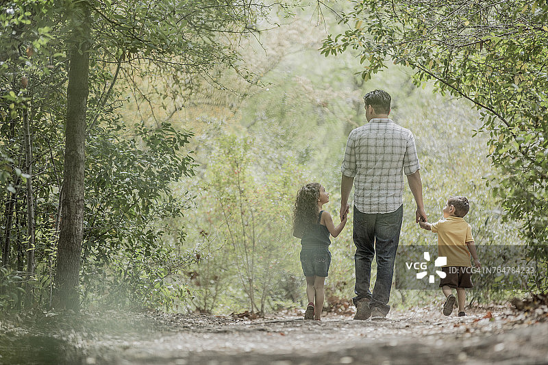 西班牙父亲带着儿子和女儿在树林里散步图片素材