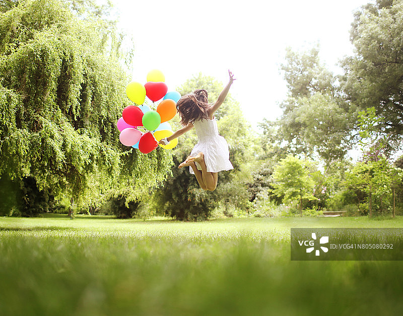 一个10岁的女孩在公园里拿着气球跳图片素材