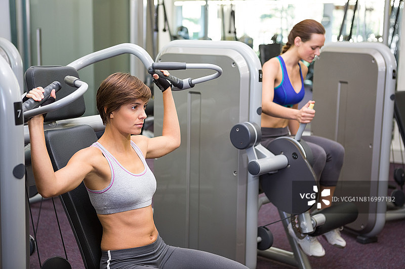 健康的黑发女子使用举重机锻炼手臂图片素材