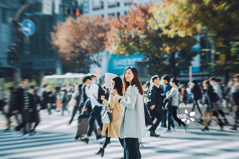 年轻女子走在斑马线上，在城市里使用智能手机图片素材
