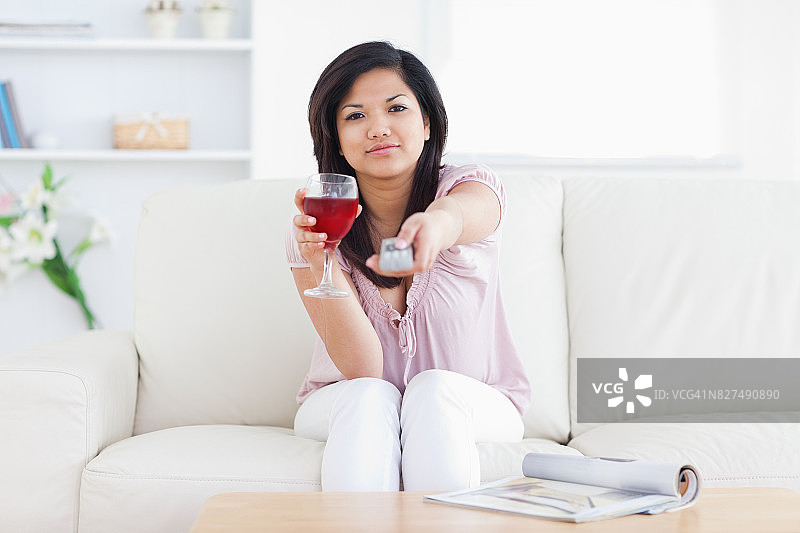 女人拿着一杯酒和一个电视遥控器图片素材