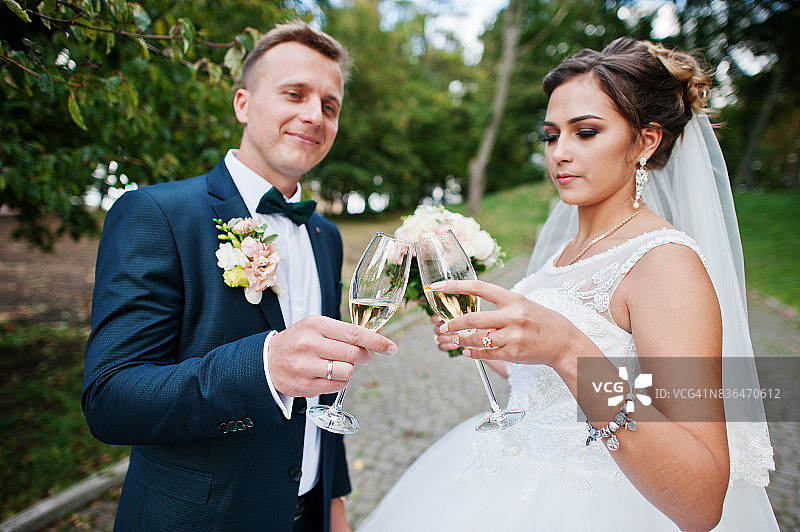 快乐的新婚夫妇在婚礼当天在公园喝香槟。图片素材