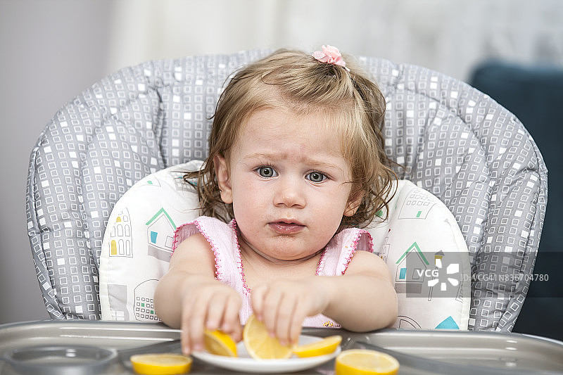快乐的小女孩在高椅子上吃柠檬。图片素材