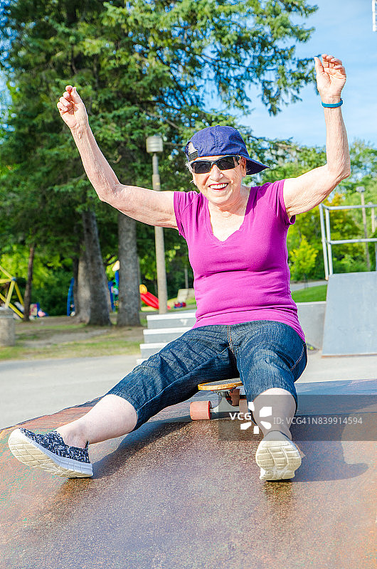 年长妇女戴着棒球帽在一边和坐在滑板顶部坡道在夏天在滑板公园图片素材