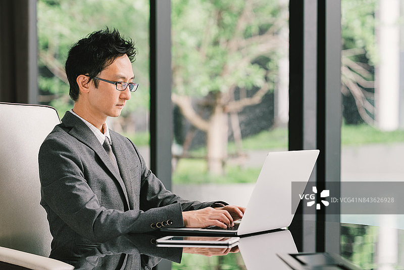 英俊的亚洲商人或企业家，在行政办公室使用笔记本电脑和数字平板电脑。领导力，商业沟通，创业，或信息技术小工具的概念图片素材
