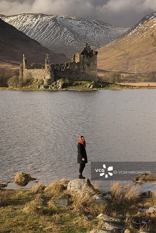 女孩站在湖边的岩石上，远处是城堡图片素材