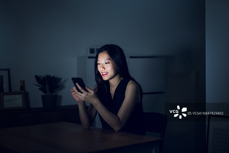 一个年轻女人在黑暗中用智能手机发短信图片素材