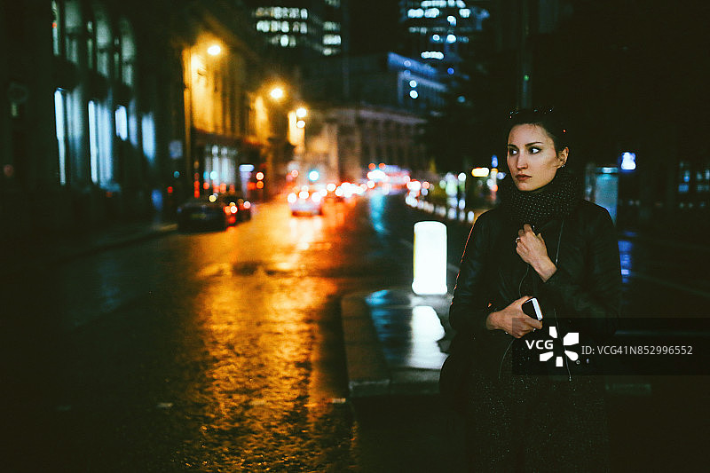 一名年轻女子在晚上走在伦敦的街道上发短信图片素材