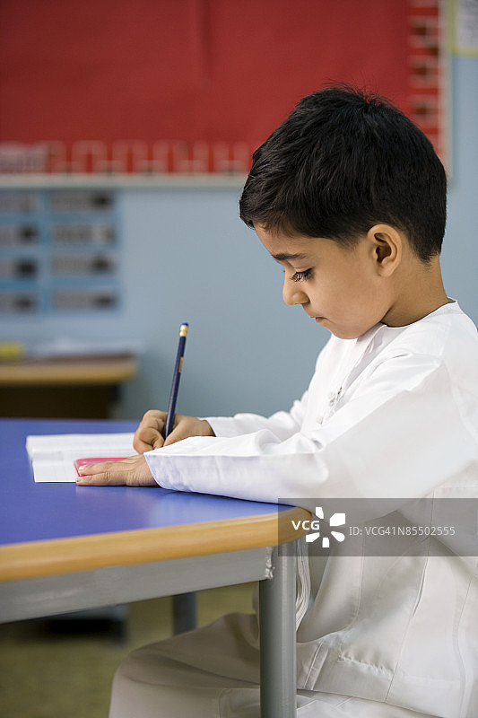 一个小男孩正在教室里做他的班级作业。图片素材