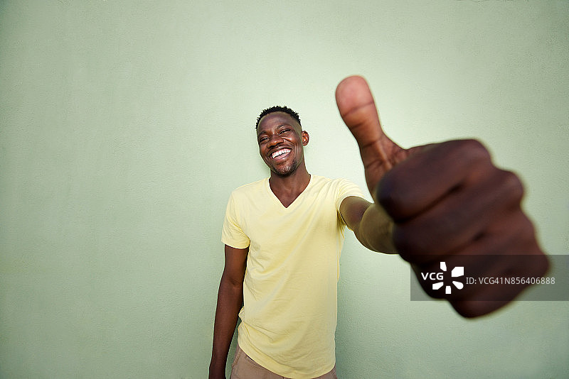 一名非洲青年在绿墙前竖起大拇指图片素材