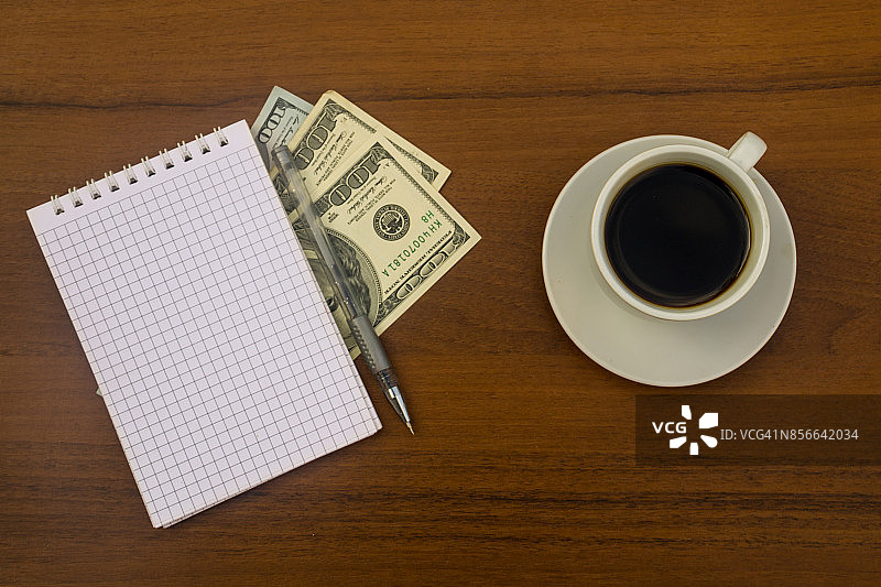 一杯咖啡，美元，笔记本和笔放在木桌上图片素材