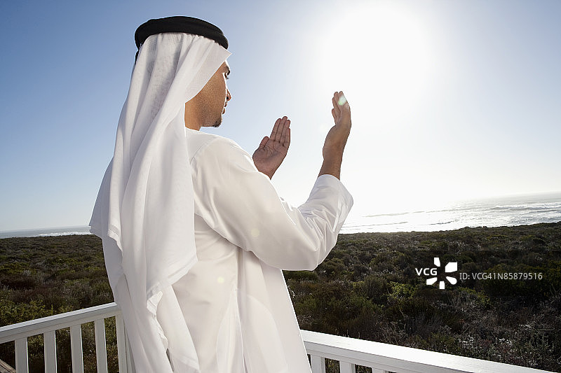 一个阿拉伯人站在阳台上祈祷。图片素材