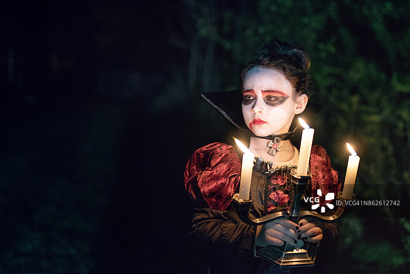 诡异的小女孩穿着万圣节的吸血鬼服装，晚上点着蜡烛图片素材