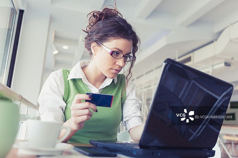 红头发的卷发女人，喝着咖啡，在当地咖啡馆用笔记本电脑用信用卡在线购物图片素材