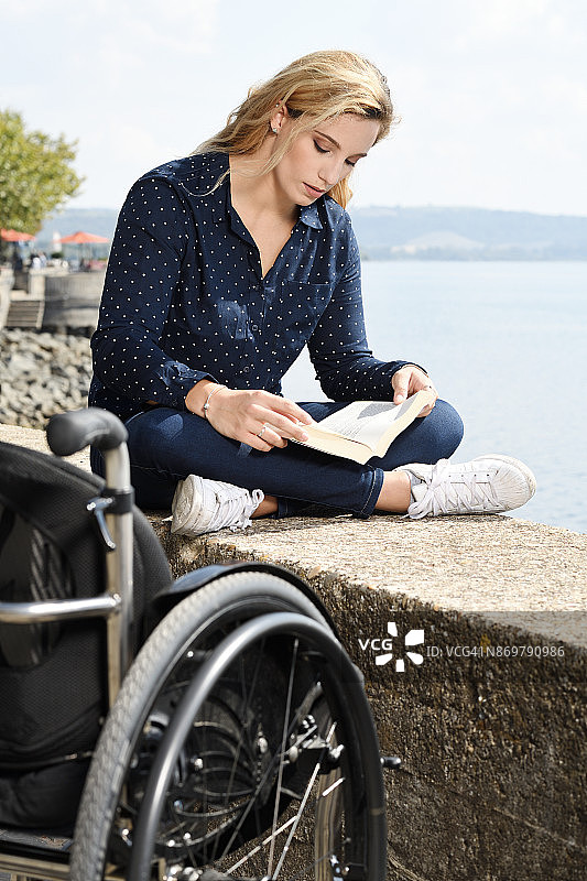 年轻女子坐着轮椅，在湖边看书休息图片素材