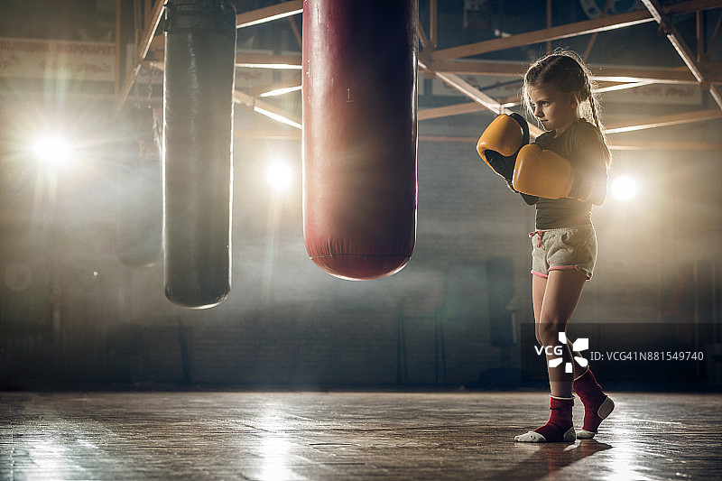 身段坚定的小女孩在体育馆进行拳击训练。图片素材
