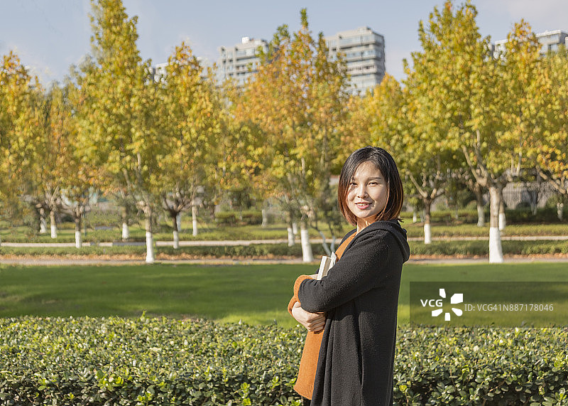 年轻的亚洲孕妇抱着书在公园里散步图片素材