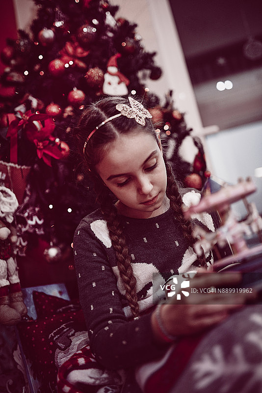可爱的小女孩坐在圣诞树下玩新玩具图片素材