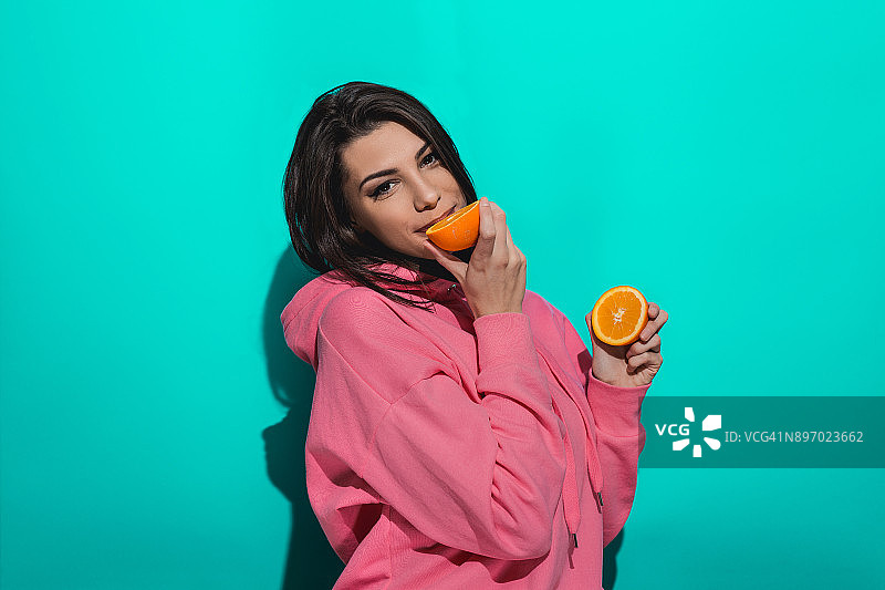 一个年轻女子拿着一个橙子，站在蓝色背景下图片素材
