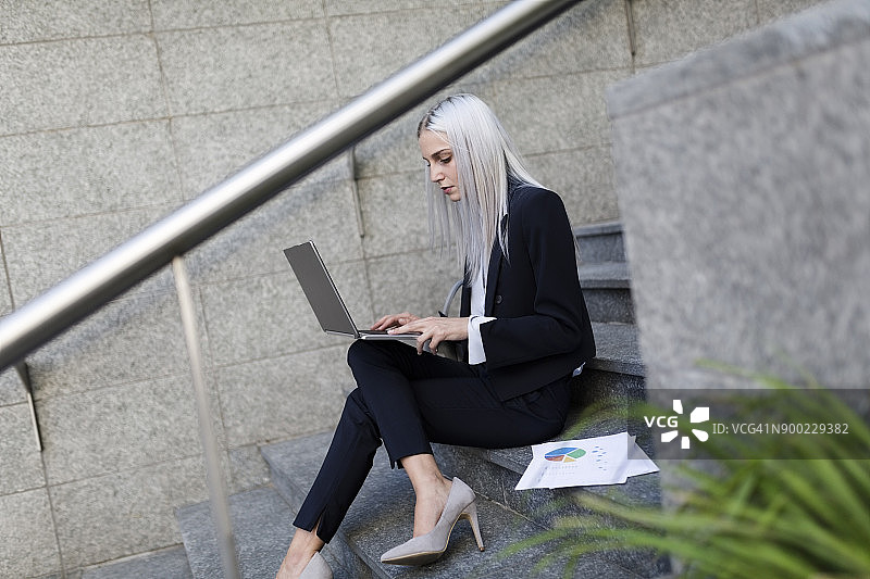 年轻的女商人坐在城市的楼梯上用着笔记本电脑图片素材