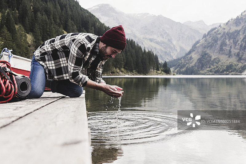 奥地利，蒂罗尔，阿尔卑斯山，一个男人跪在码头上从山上的湖里舀水图片素材