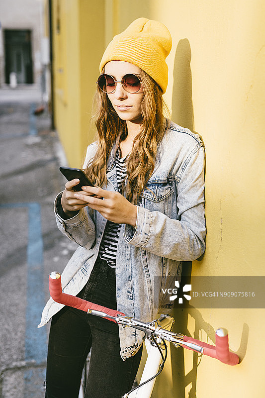 肖像的时尚年轻女子与自行车靠在正面使用手机图片素材