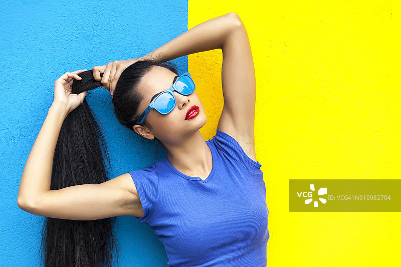 戴着蓝色太阳镜的女人站在彩色的墙前图片素材