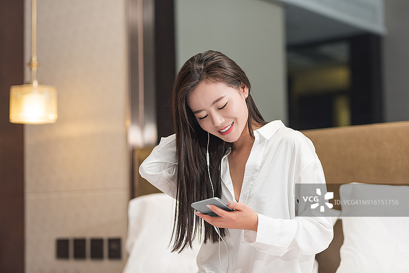 微笑的女人在床上用耳机和智能手机听音乐图片素材