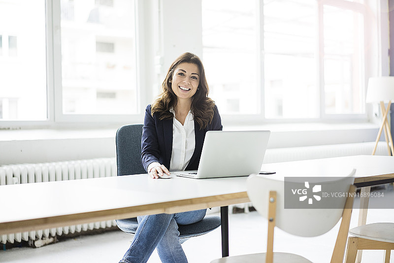 一个快乐的女商人坐在办公室的办公桌前用笔记本电脑工作图片素材