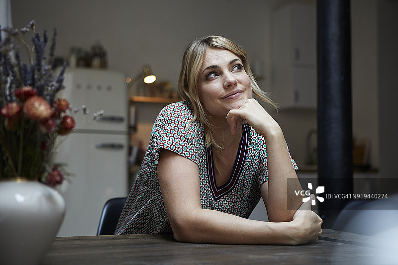 微笑的女人坐在餐桌旁思考的肖像厨房图片素材