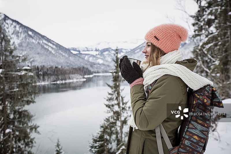年轻女子与热饮站在高山冬季景观与湖泊图片素材