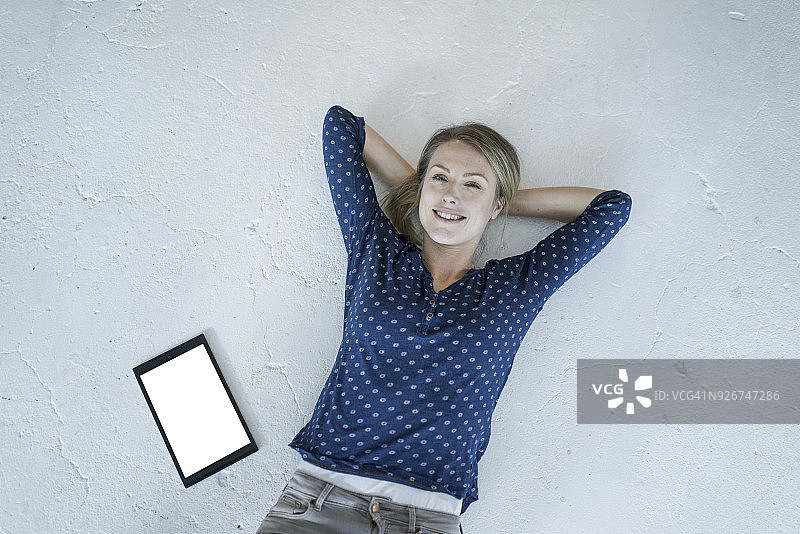 一个微笑的年轻女子的肖像躺在地板上，手里拿着平板电脑图片素材