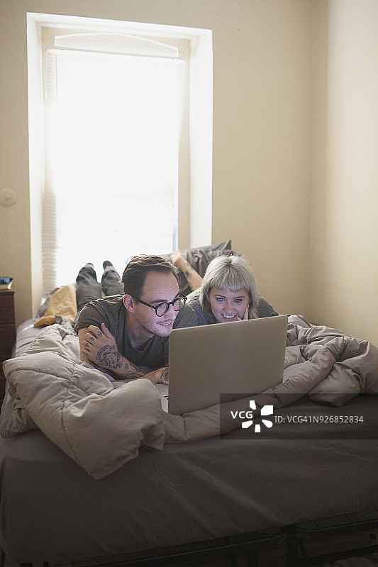 一对年轻夫妇躺在床上看笔记本电脑图片素材