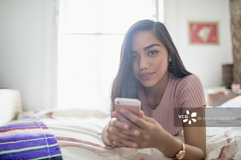 年轻女子在床上用智能手机图片素材
