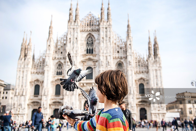意大利伦巴第米兰，男孩在米兰大教堂广场喂鸽子图片素材