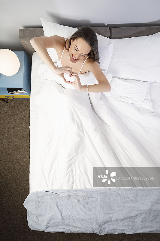 睡美人画像美丽的年轻女子在床上用手做心形自然的生活方式图片素材
